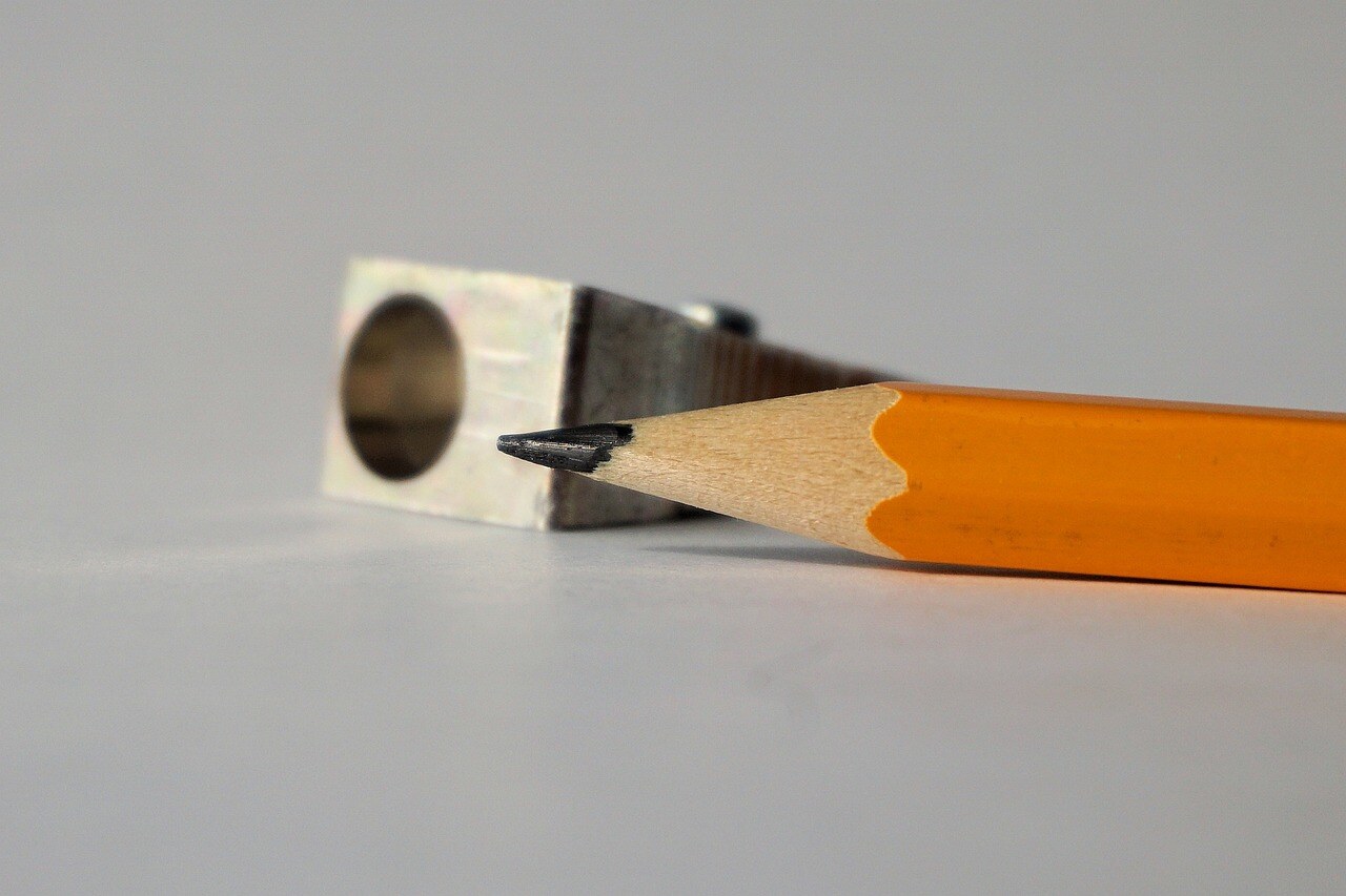A picture of the tip of a sharpened pencil next to a hand-held pencil sharpener. 
